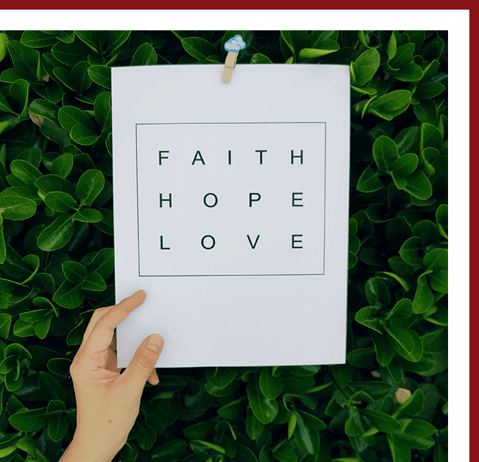 A hand holding onto a paper with faith, hope and love written on it.